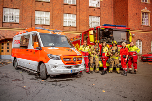 Ambulans, brandbil och räddningspersonal på brandstationens gård.