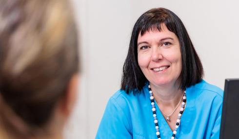 En kvinna bakom en dator pratar med en patient.