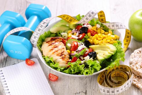 Food on a plate. On the table next to the plate, newspapers, dumbbells, tape measure, rice cakes and an apple.